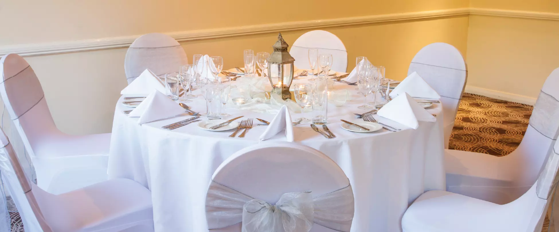A table made up for a wedding with white table covers, chair covers and centrepiece..